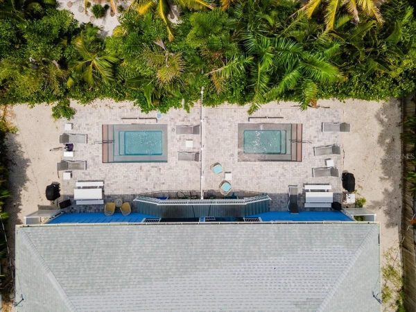 Aerial view of a terrace with two rectangular pool tubs flanked by lounge chairs and palm trees beside a blue-roofed building.