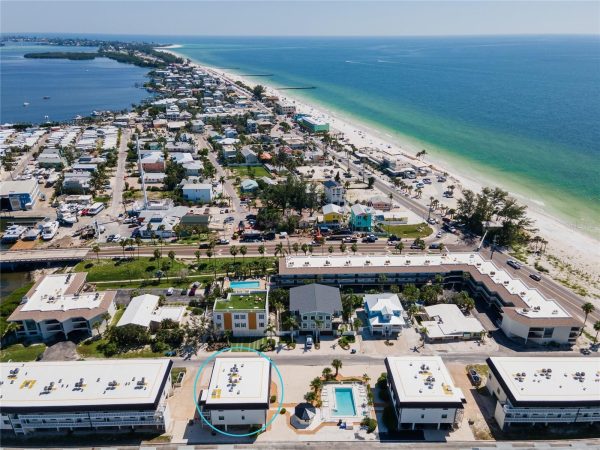 Aerial view of a coastal town with the ocean on the right; circled building is a white two-story property with a flat roof and small front pool area.