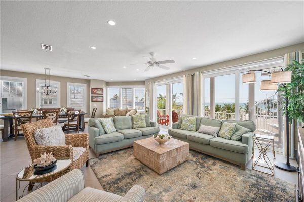 Bright coastal living room with pastel sofas, a woven coffee table, and ocean view through large glass doors.