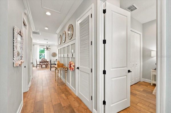 Bright hallway in a modern home with light gray walls, white wainscoting, and a row of clocks along the wall leading to a dining area.