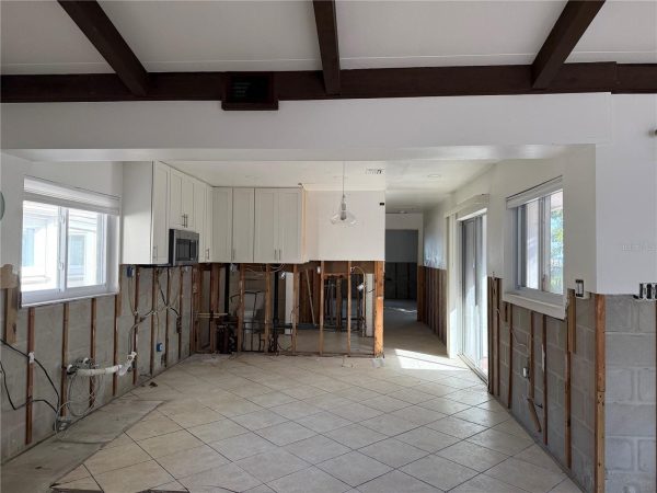 Kitchen under renovation with exposed wall studs, white cabinets installed, and large windows letting in light.
