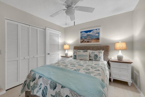 Coastal-themed bedroom with a wicker-headboard bed, seashell quilt, teal throw, and two white nightstands with lamps.",