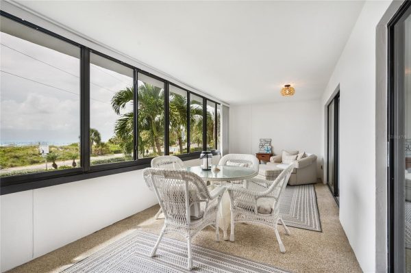 Coastal screened porch with white wicker dining set and glass table, overlooking palm trees and the beach outside