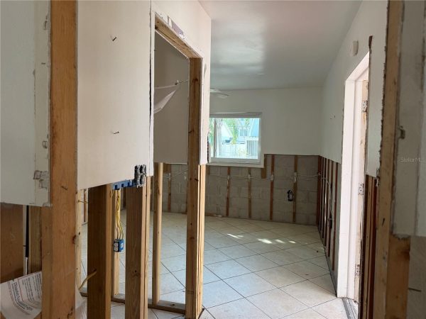 Kitchen under renovation with exposed wooden studs, removed cabinets, and hanging drywall panels; tiled floor and a window at the back providing daylight.