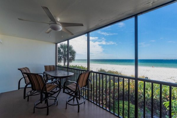 Screened balcony with a round table and four striped chairs overlooking a sandy beach and turquoise sea.