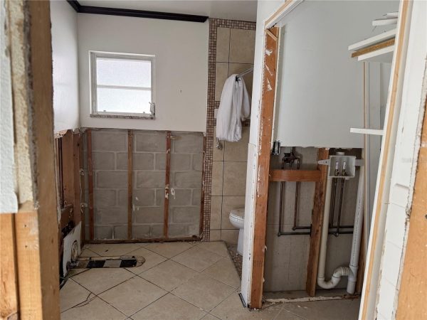 Bathroom under renovation with exposed studs, pipes, and a toilet visible next to a window.