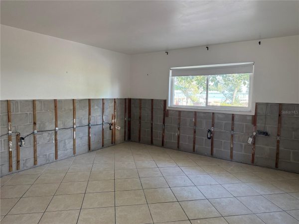 Room with half-wall exposed: studs, concrete block base, and visible wiring, likely a kitchen under renovation with a window letting in natural light.