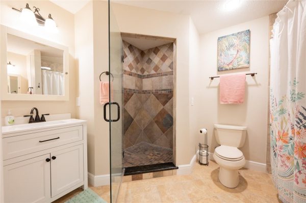 Bathroom with glass-enclosed tiled shower, white vanity, and pink hand towel by the sink.