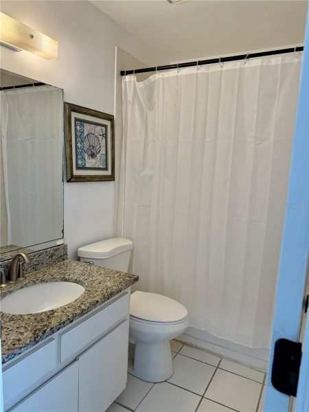 Bathroom with granite countertop vanity, sink, mirror, framed sea-themed art, toilet, and white shower curtain.