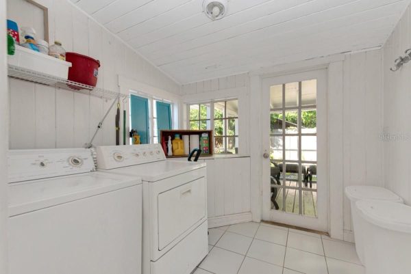 Laundry room with a top-loading washer and a dryer, white walls, and a glass-paned door to the outdoors to the right.