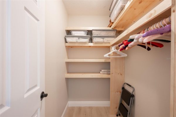 Narrow closet with unfinished wood shelves, clear bins of linens on the top, and colorful hangers on the right.