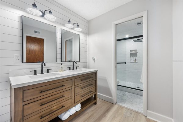 Double vanity with two sinks and dark metal faucets on a white countertop, wood cabinet, and white shiplap wall behind.