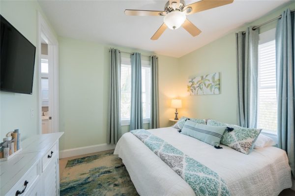 Cozy coastal bedroom with mint-green walls, queen bed in white quilt and teal accents, and three windows with blue curtains.
