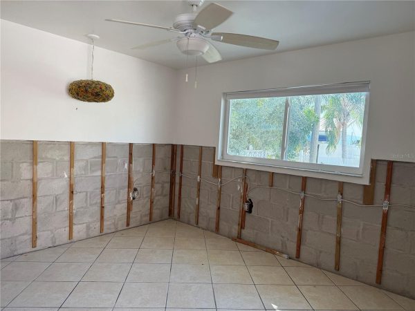 Renovation scene: room with exposed studs and lower concrete block walls, a large window, and a ceiling fan overhead.