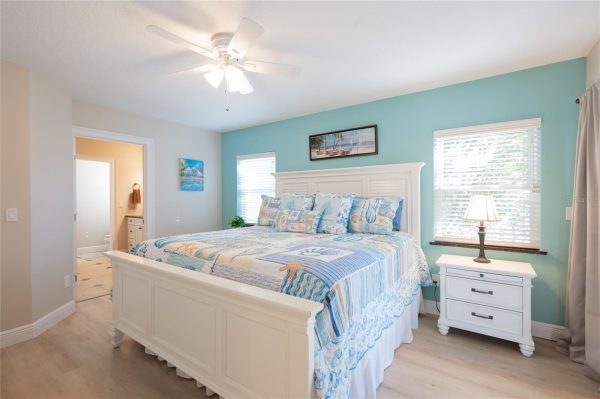 Coastal-style bedroom with a white wooden bed, turquoise wall, two windows, and a white nightstand lamp.