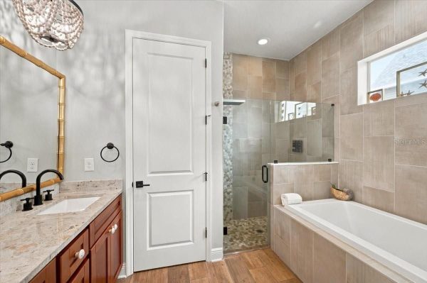 Modern bathroom with a double vanity, granite countertop, and black fixtures; glass shower and bathtub with beige tile walls.