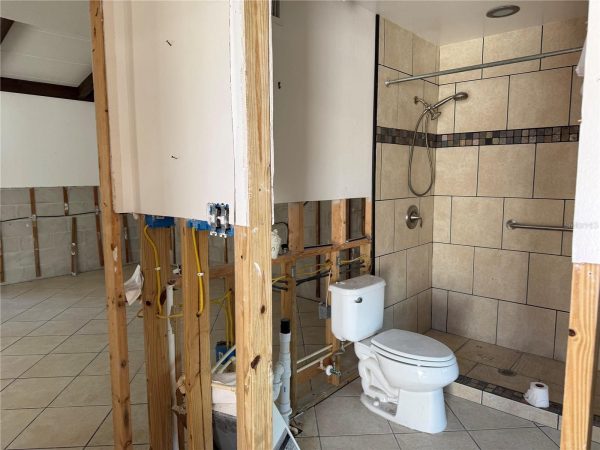 Bathroom under renovation with exposed studs, wires, and plumbing; toilet installed next to a tiled shower stall.