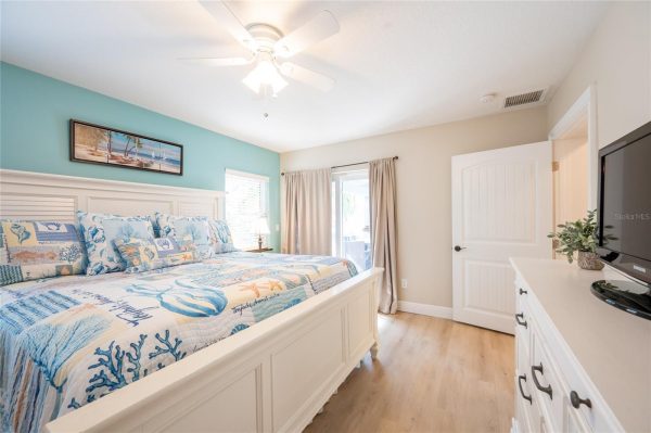 Coastal bedroom with a white bed, teal accent wall, and ocean-themed quilt; dresser and TV nearby.