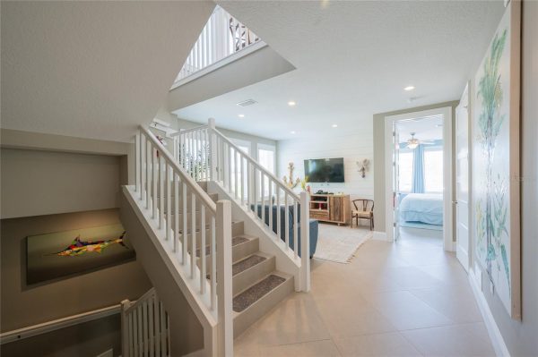 Open foyer with a white staircase and railing leading to the living room; a TV and coastal decor visible.