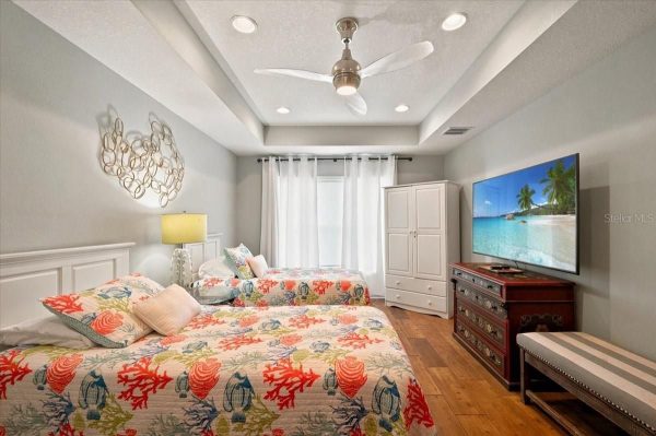 Twin bedroom with nautical bedding, white furniture, and a ceiling fan; TV on dresser across from the beds.