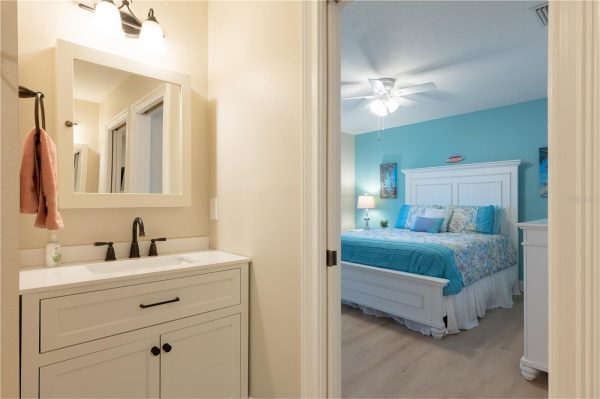Bathroom vanity with white cabinet and mirror, pink towel, and soap; doorway to a teal-bedroom. (informative)