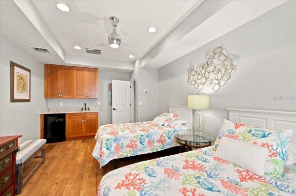 Coastal-themed hotel room with two twin beds, coral and seashell bedding, wooden floor, and a small kitchenette area in the corner.