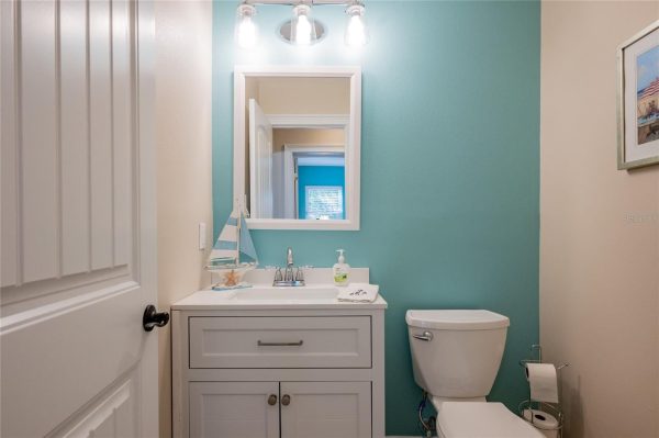 Small bathroom with a white vanity, teal wall, and mirror reflecting a blue room beyond the door