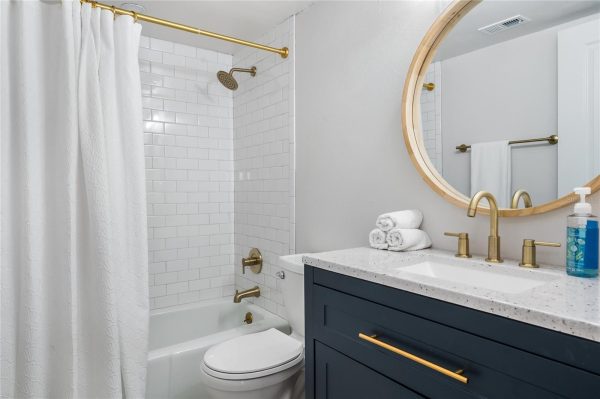 White subway-tiled shower with brass fixtures beside a navy vanity and a round wooden-framed mirror above the sink.