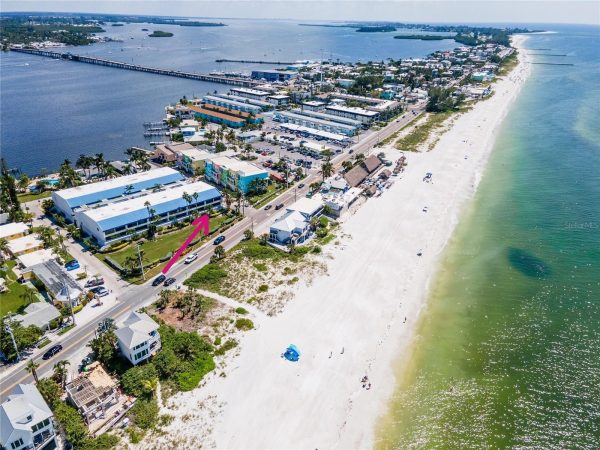 Aerial view of a beach town with a long white-sand shoreline; pink arrow highlights a blue-roofed building along the road.