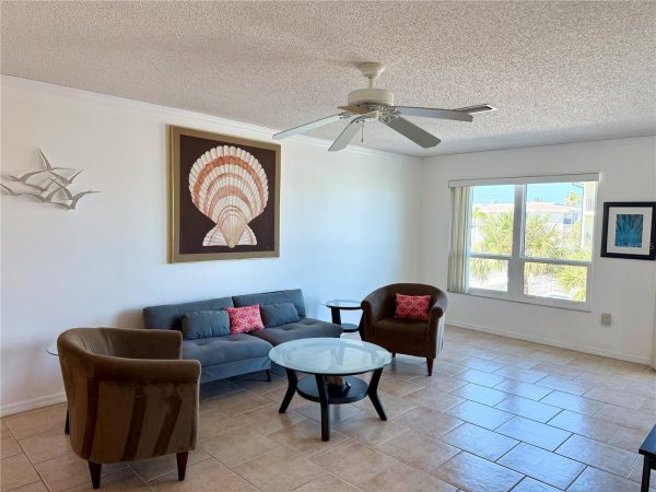 Cozy living room with a blue sofa, two brown chairs, glass coffee table, and coral shell wall art under a ceiling fan.