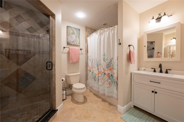 Bathroom with glass-enclosed shower on the left, tropical-pattern shower curtain, toilet, and white vanity with a black faucet and mirror.