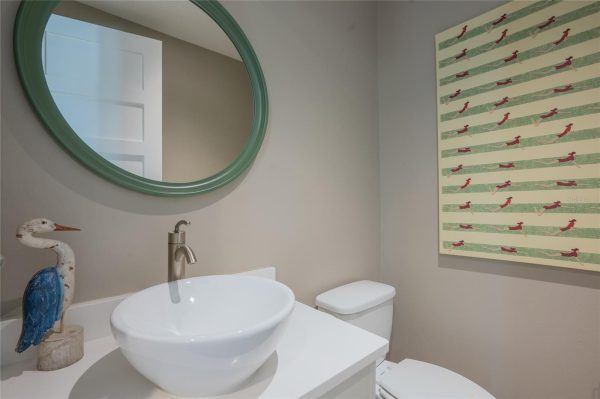 Bathroom vanity with round white vessel sink, brushed-nickel faucet, and a green circular mirror; a pelican statue on the counter.