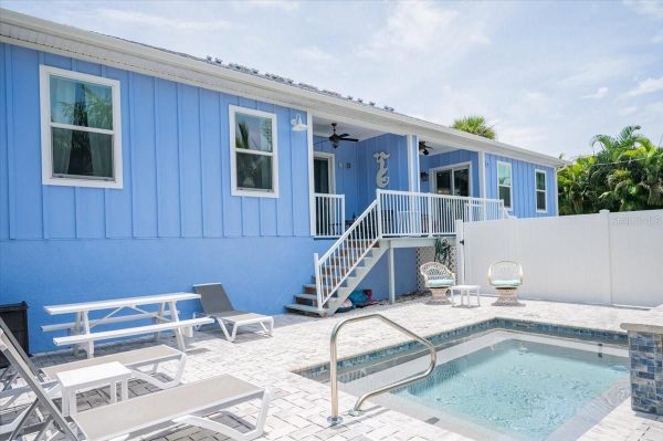 Backyard of a blue house with a rectangular pool, white patio furniture, and a stairway to a second-floor deck.