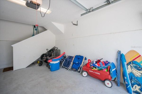 Garage storage under a stairwell with a blue cooler, folding chairs, a red Radio Flyer wagon, and surfboards leaning against the wall.