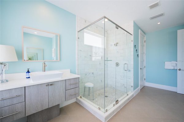 Bright modern bathroom with blue walls, a glass-framed shower, white marble tiles, and a gray wood vanity with a rectangular sink.