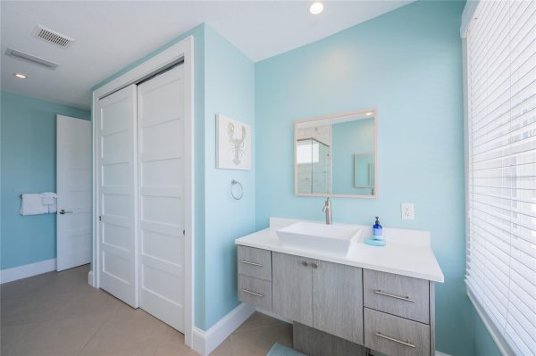 Bathroom with light turquoise walls, floating vanity, rectangular sink, and wall mirror by a large window with blinds