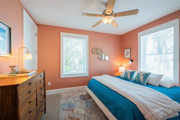 Bright coral-walled bedroom with white trim, a wooden dresser on the left, and a ceiling fan above a turquoise bed.