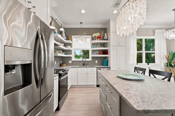 Modern white kitchen with a stainless steel side-by-side refrigerator, open shelves, and a large island centerpiece.