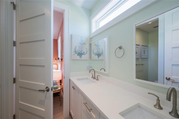 Bright bathroom with white double vanity, silver faucets, pale green walls, and coral artwork above the sink.