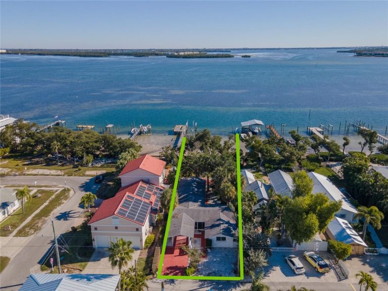 Aerial view of a waterfront neighborhood with two long green-outlined lots running between houses toward the water and boat docks in the background.