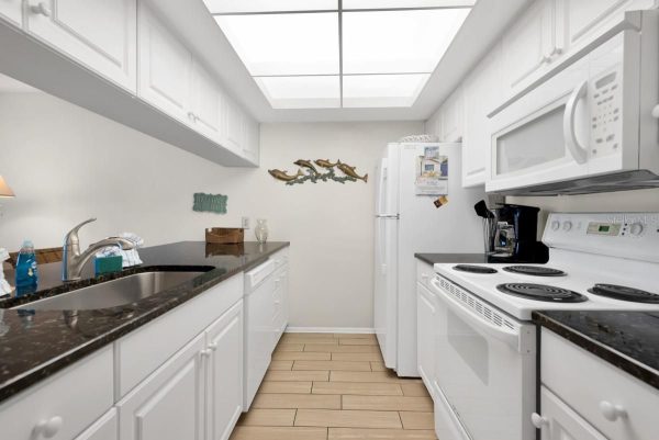 Bright white galley kitchen with black granite counters, sink on the left and stove on the right under a skylight.