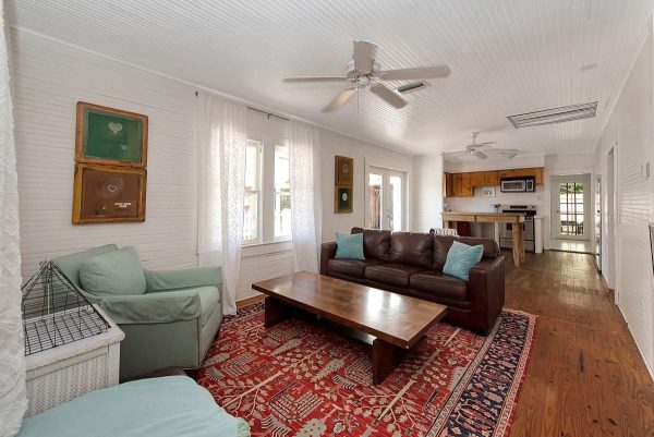 Bright living room with white beadboard walls, two turquoise chairs, a brown leather sofa, a wooden coffee table, and a red patterned rug.