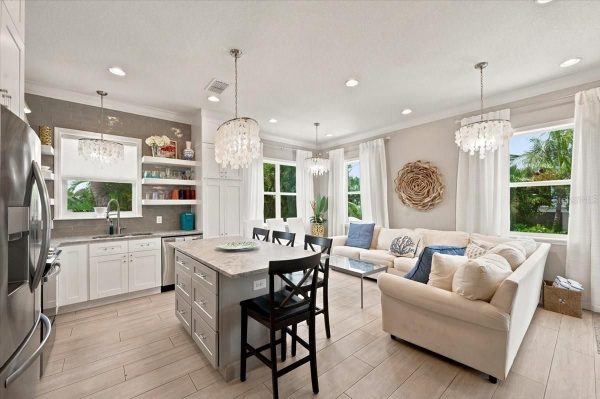 Open-concept kitchen and living room with white cabinets, marble island, and crystal pendant lights nearby the sofa area.