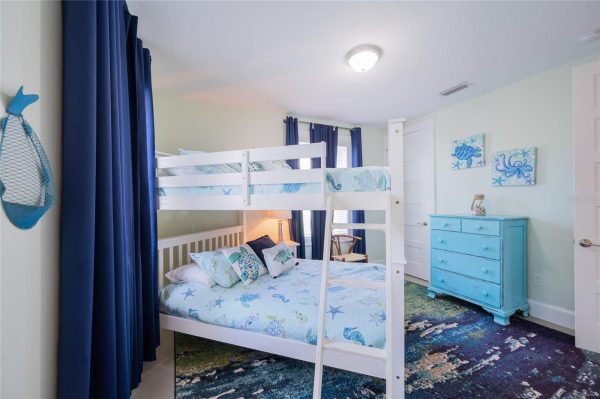 Coastal-themed children's bedroom with a white bunk bed over a full-size bed, navy curtains, and a blue dresser against pale walls.