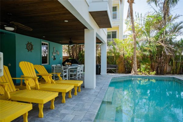 Poolside patio with bright yellow Adirondack chairs, turquoise wall, and a dining table under a wooden ceiling.