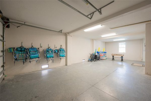 Spacious garage with white walls; blue striped beach chairs mounted on the left wall and a cart with pool floats and inflatables in the back right corner, plus a foosball table nearby.
