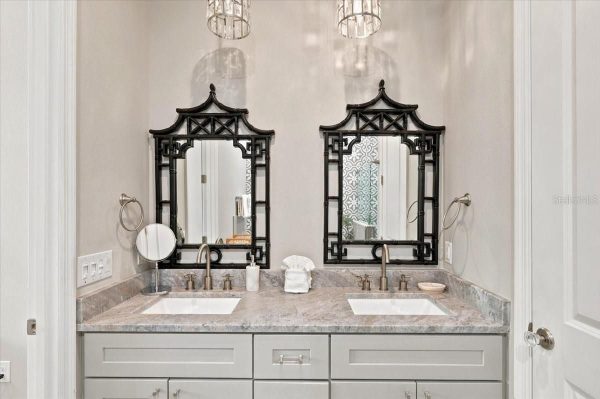 Dual sink vanity with gray cabinets and marble countertop, flanked by two black decorative lattice mirrors and chrome fixtures.
