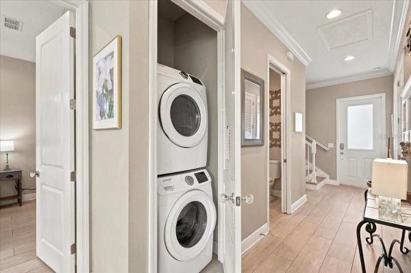 Stacked front-loading washer and dryer in a laundry closet along a light beige hallway.
