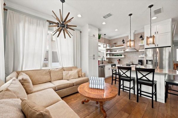 Open-concept living area with a beige sectional sofa, round wooden coffee table, and a white kitchen island with four black barstools.
