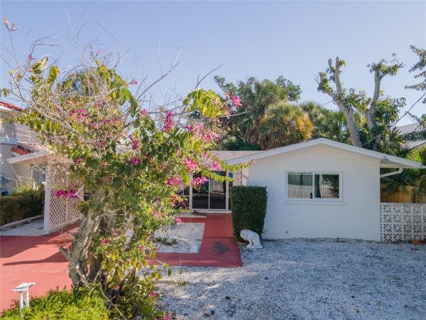 White single-story house with a pink bougainvillea bush in bloom in the front yard and a red walkway.